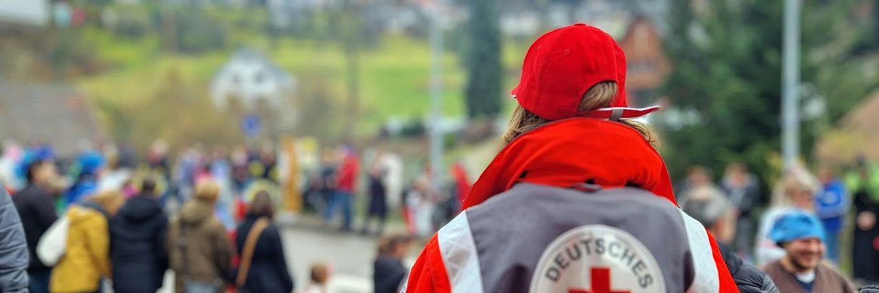 Helferin in Einsatzkleidung die von hinten gezeigt auf einen Fasnachtsumzug schaut